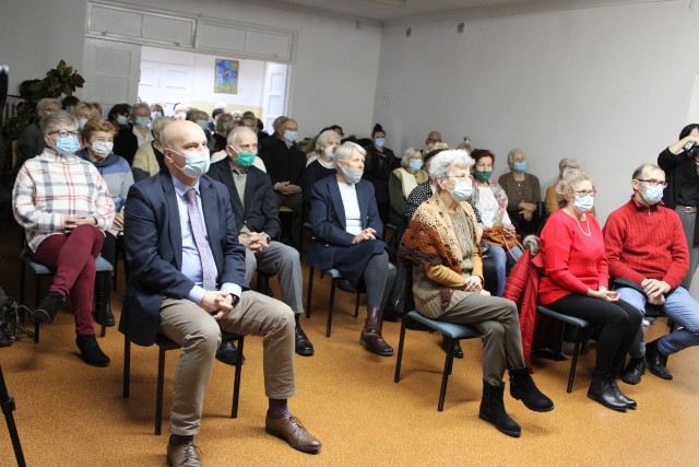 Publiczność w maskach siedząca na krzesłach w niewielkiej sali