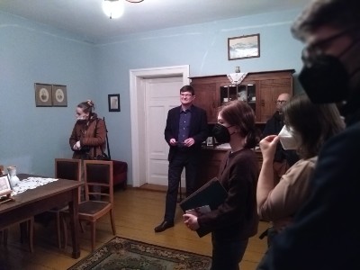 Gabinet Hulki Laskowskiego, mężczyzna na tle niebieskiej ściany, po prawej stronie stoikilka osób zwróconych profilem do fotografującego