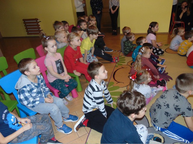 Grupa przedszkolaków siedzących na podłodze i oglądających przedstawienie