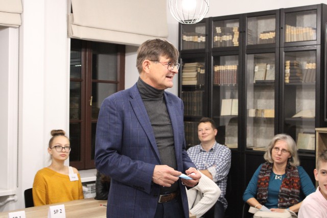 Trzy osoby siedzą za stołem, mężczyzna stoi i przemawia