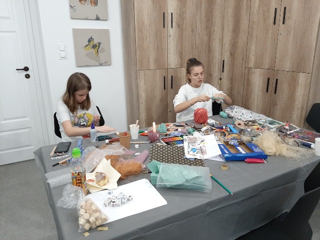 Dwie dziewczyny siedzą przy stole z materiałami plastycznymi i tworzą prace
