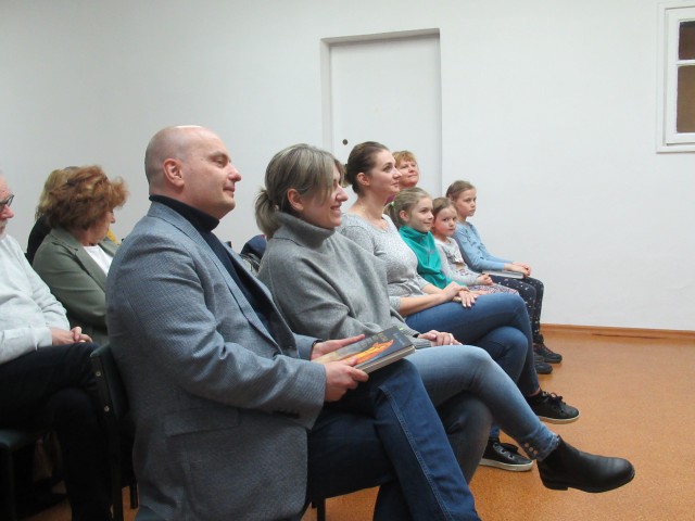 Siedzący na krzesłach ustawionych w rzędzie dorośli i dzieci